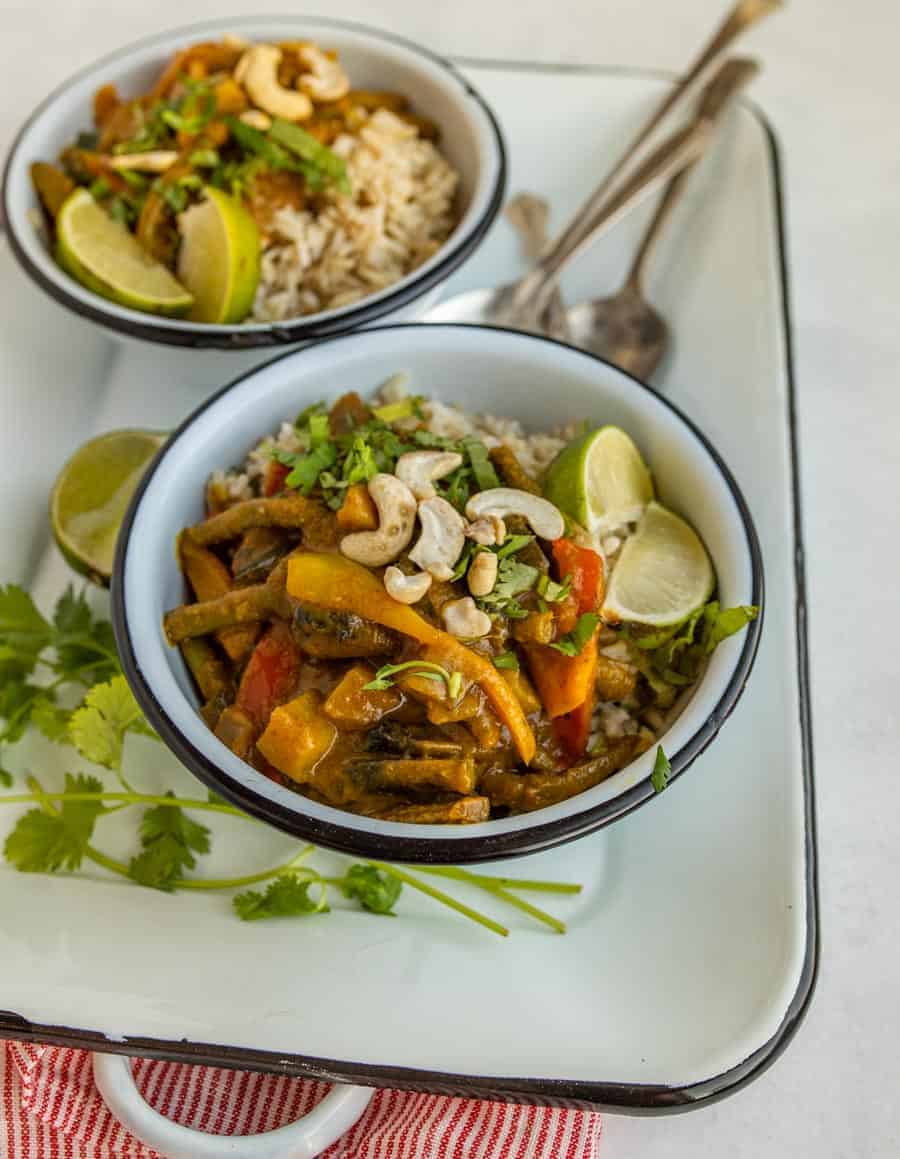 two bowls of a vegetable curry with spoons on a white tray.