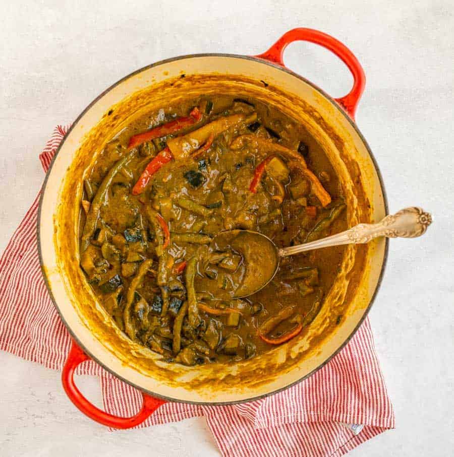 one red pot of veggies and curry with a silver spoon.