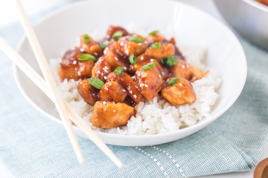 general tso's chicken with white rice in white bowl with chopsticks.