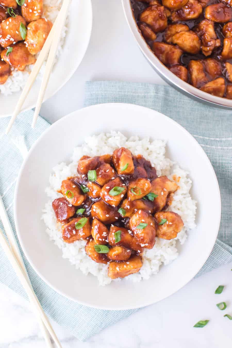 General Tso's chicken with white rice on white dish with skillet of general tso's.