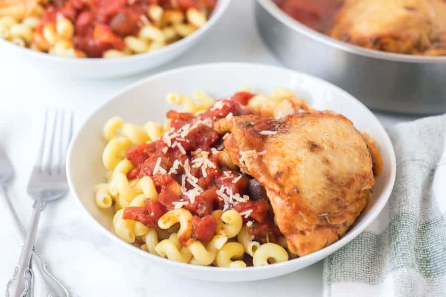 tomato and garlic pasta with chicken thigh in white bowls with forks.
