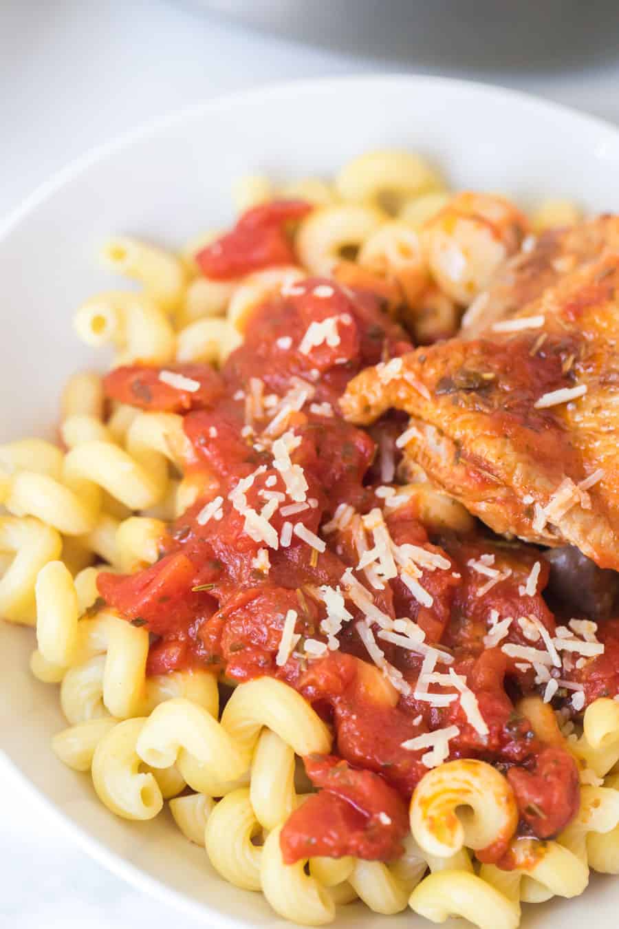 chicken with pasta and tomatoes in a white bowl.