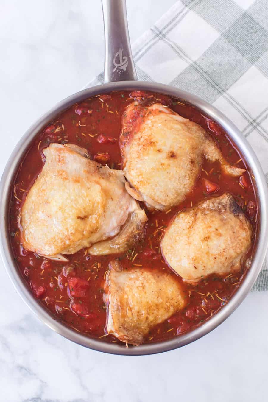 close up of chicken thigh roasting in the tomato sauce in stainless pan.