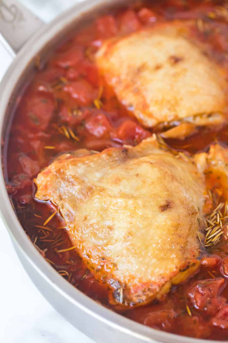 close up of chicken thigh roasting in the tomato sauce in stainless pan.