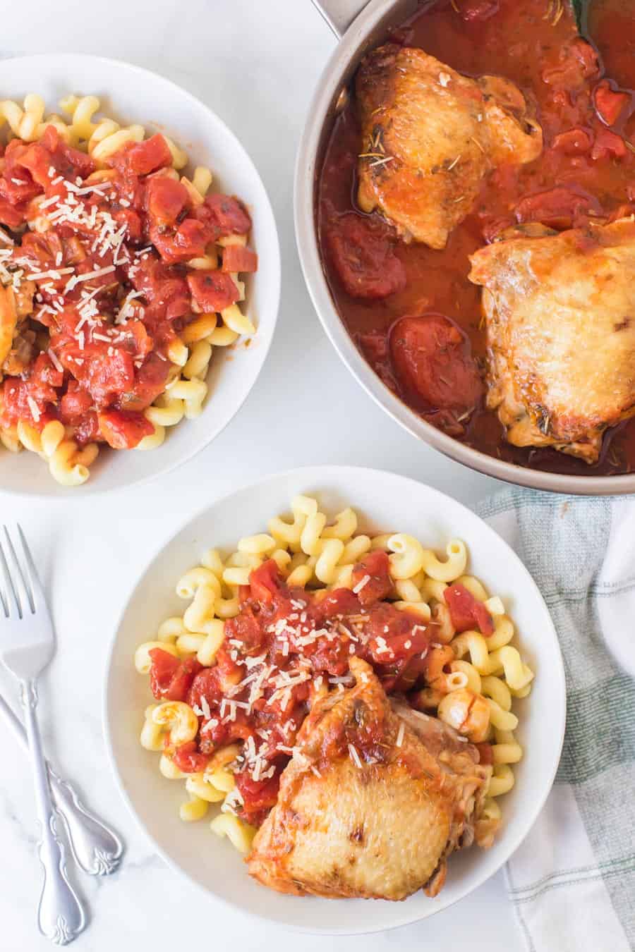 chicken with tomato sauce over garlic twisty pasta in a white bowl top view.