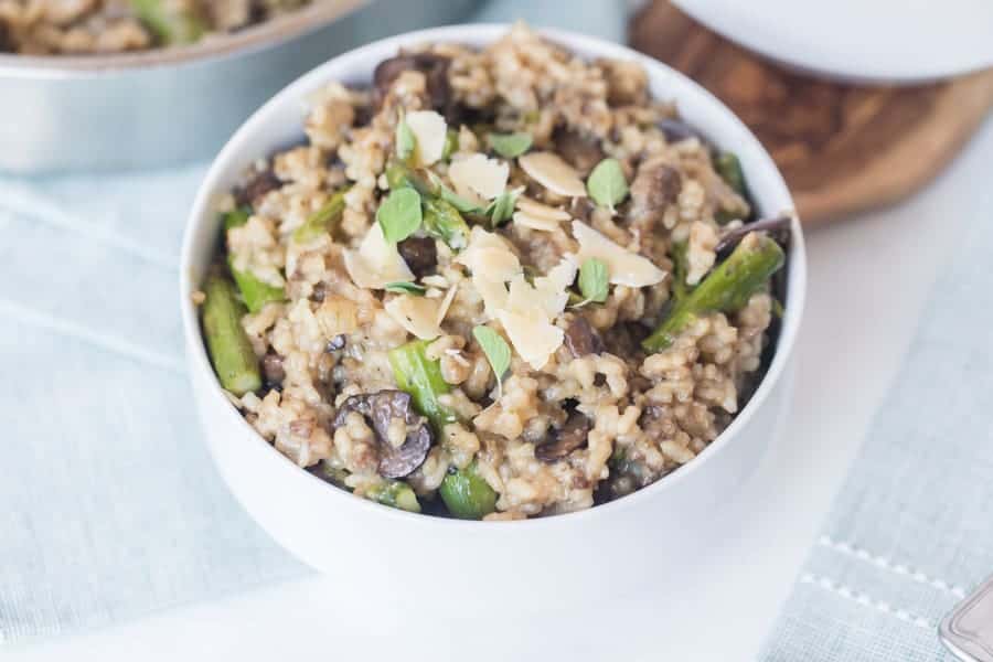 Risotto in a white bowl with asparagus and parmesan on top.