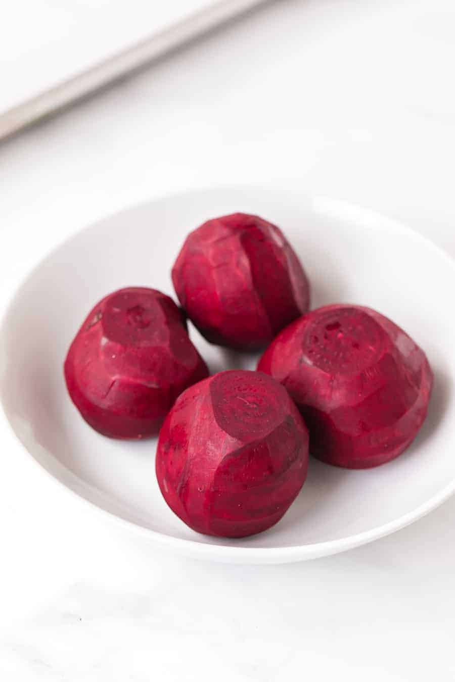 skinned uncooked beets in round white bowl.