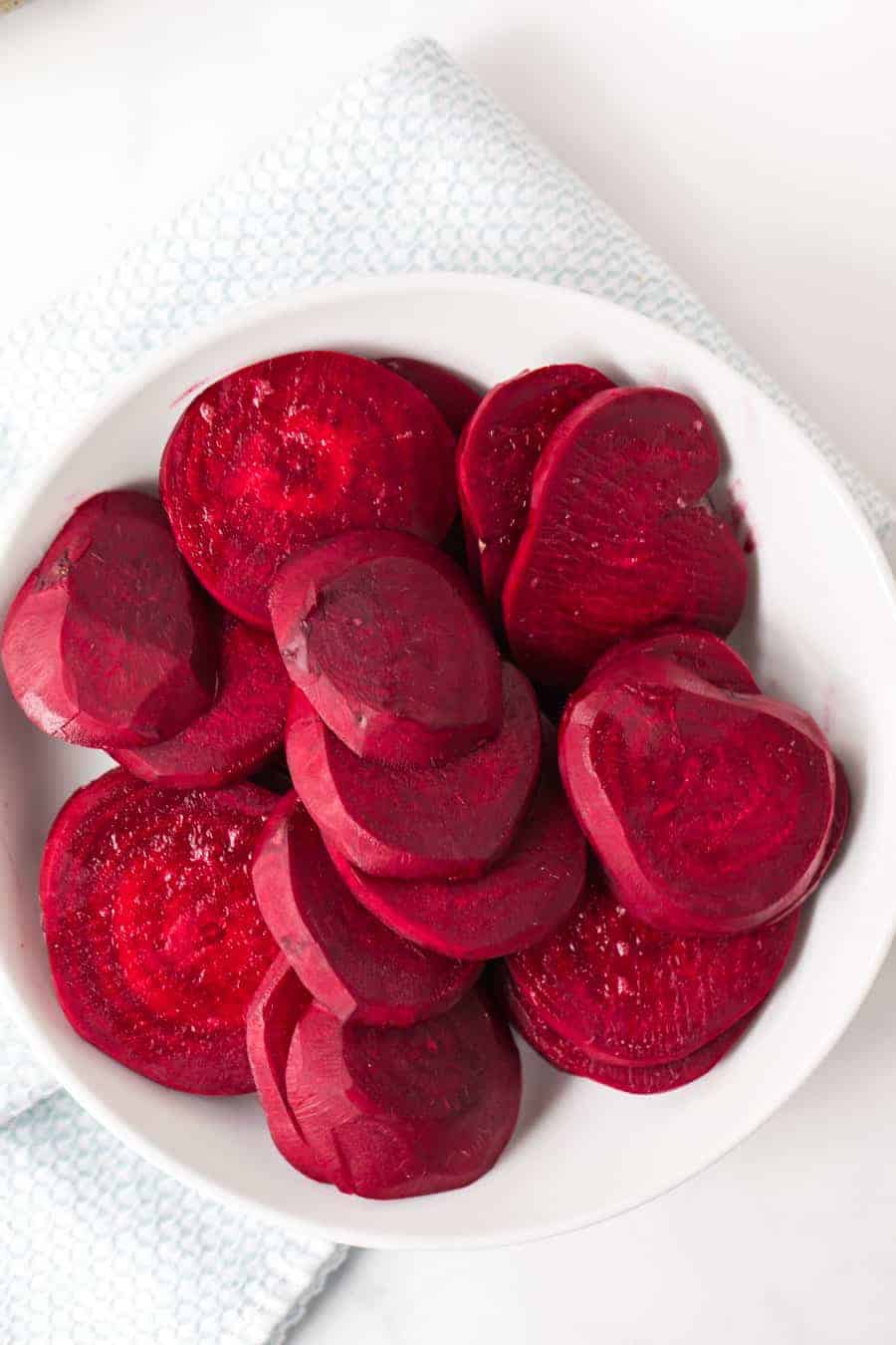 a bowl of piled up raw red beets sliced into thin rounds.