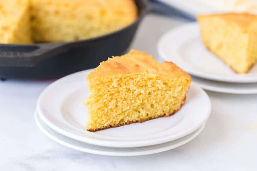 one slice of cut cornbread on a white plate ready to eat.