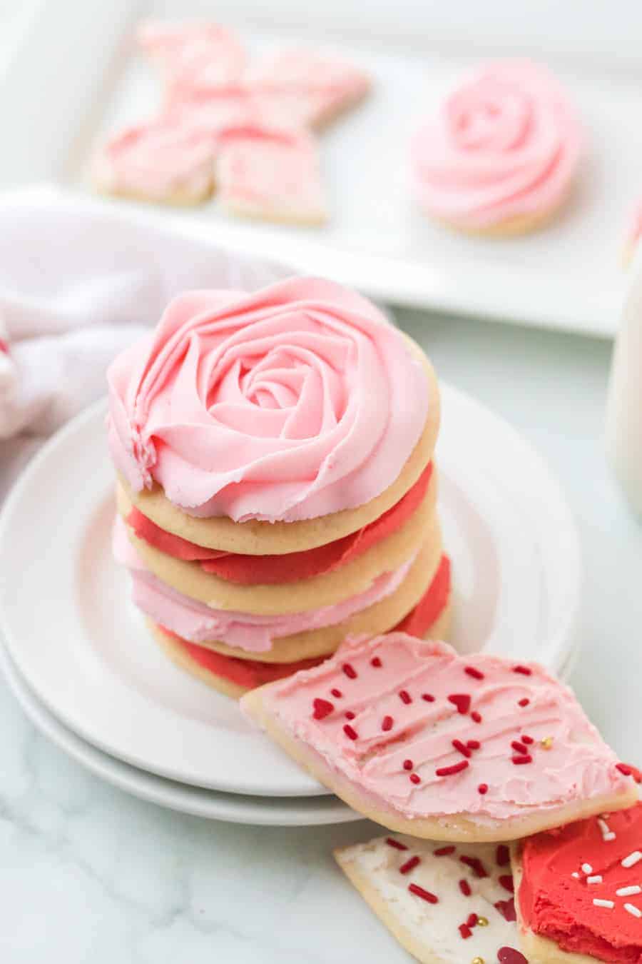stack of iced valentine's sugar cookie cutouts on round white plates.