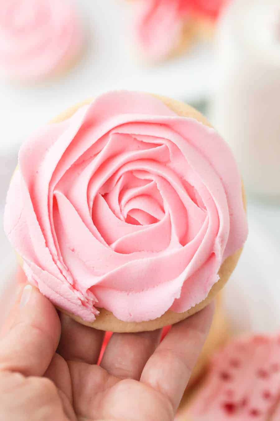 woman holding iced sugar cookie cutout with pink rose icing.