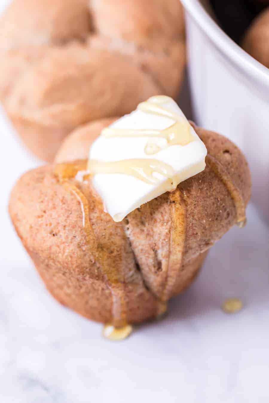 clover rolls with pat of butter and drizzled with honey on white surface.