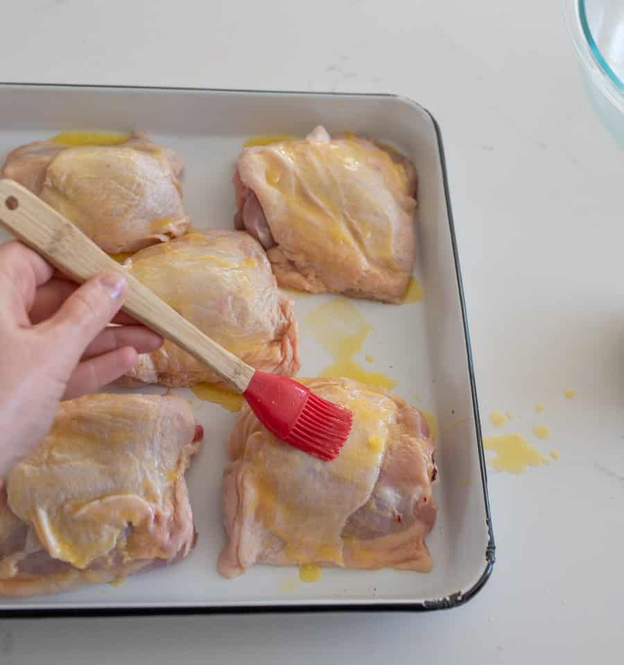 brushing oil onto chicken thighs on a baking dish.