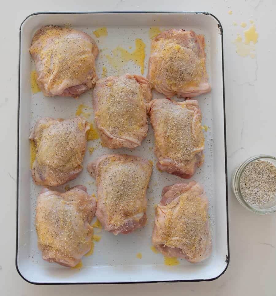 top view raw chicken thighs covered in seasoning on a baking dish.