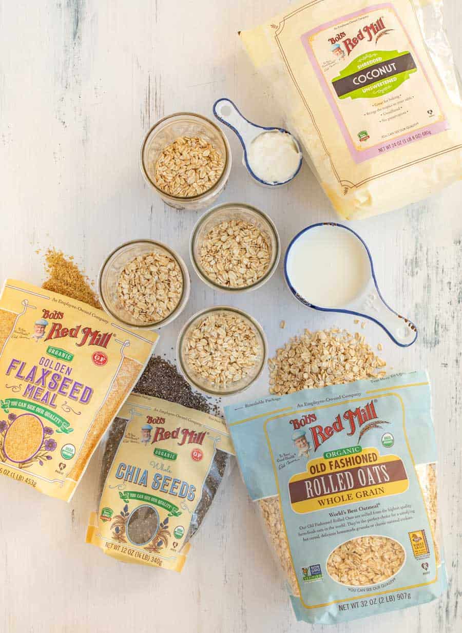 Bob's Red Mill ingredients like flax seed mill, chia seeds, rolled oats, and coconut are bagged around mason jars ready to make overnight oats.