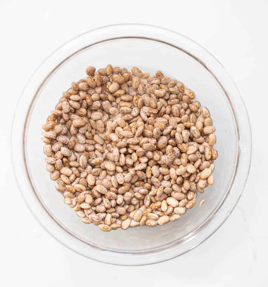 Top view of white beans in a clear glass bowl on white countertop.