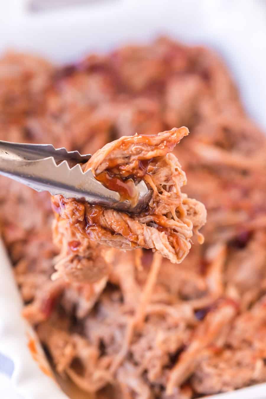 tongs crimping onto shreds of BBQ pulled pork.
