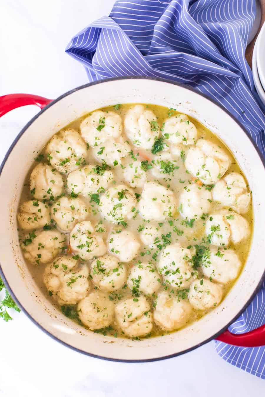 dumplings and soup in a dutch oven on blue and white striped towel.