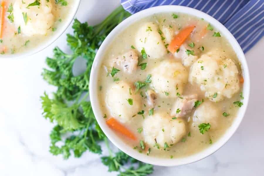 Top view of a small white round bowl of chicken and dumplings soup on a be of parsley.