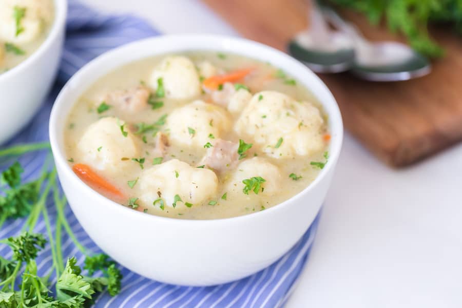 white bowl filled with old fashioned chicken and dumplings on blue and white striped towel with garnish.