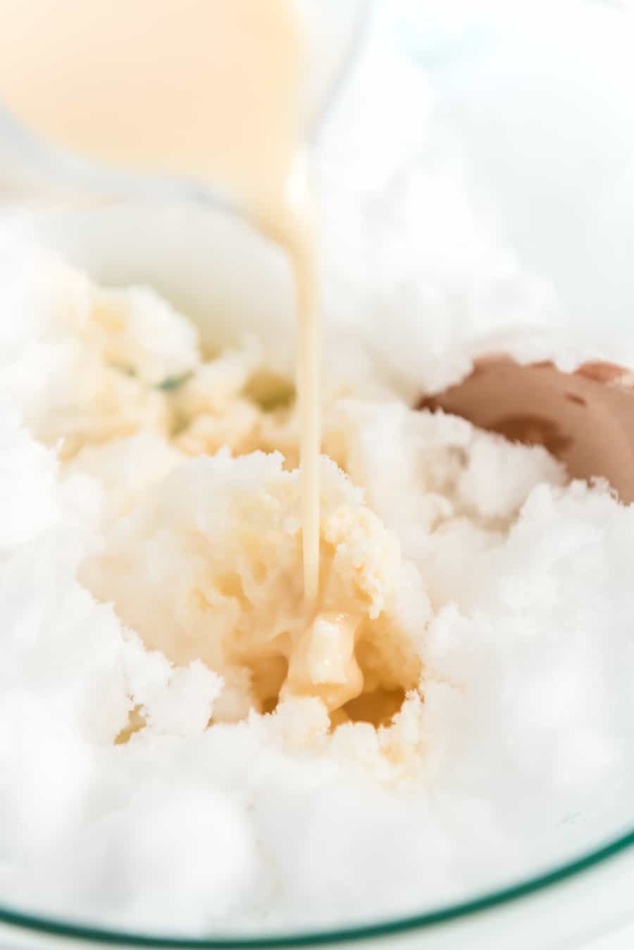 milky cream mixture being poured over a bowl of white snow.