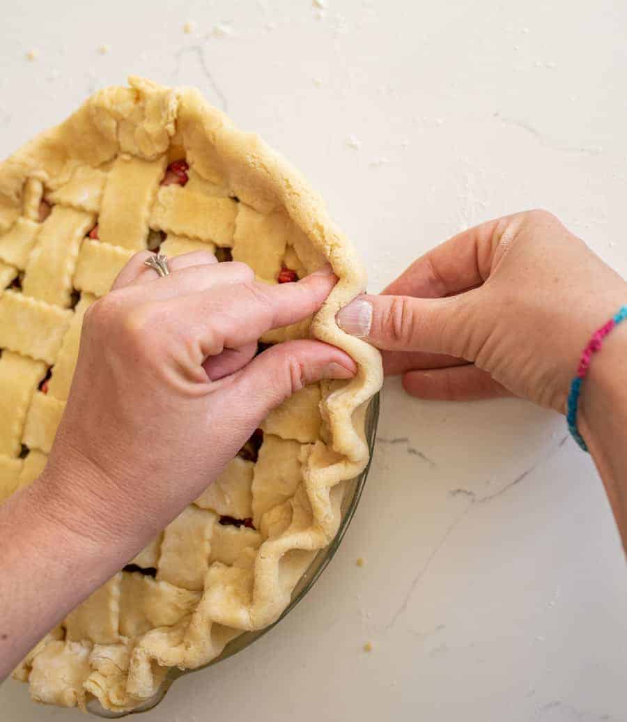 Hands pinching the outside dough of pie crust together.