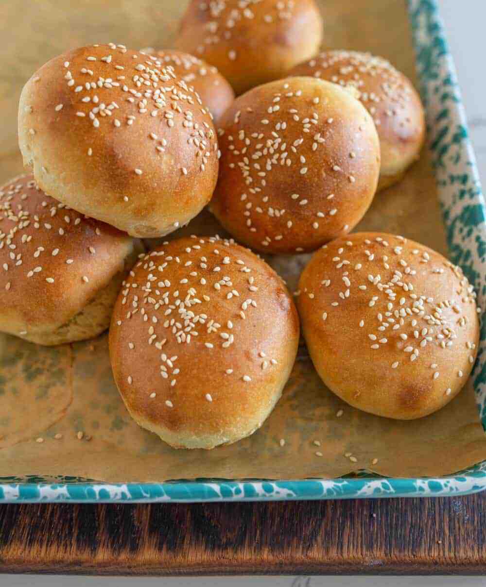 Sourdough burger buns on a blue and white enamel sheet after baking.