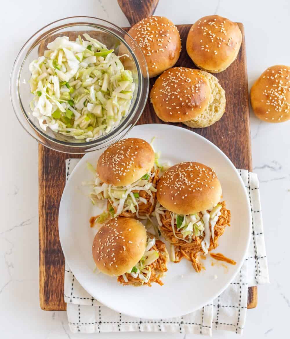 Sourdough buns with BBQ chicken and shredded cabbage on them sitting on a wooden cutting board.