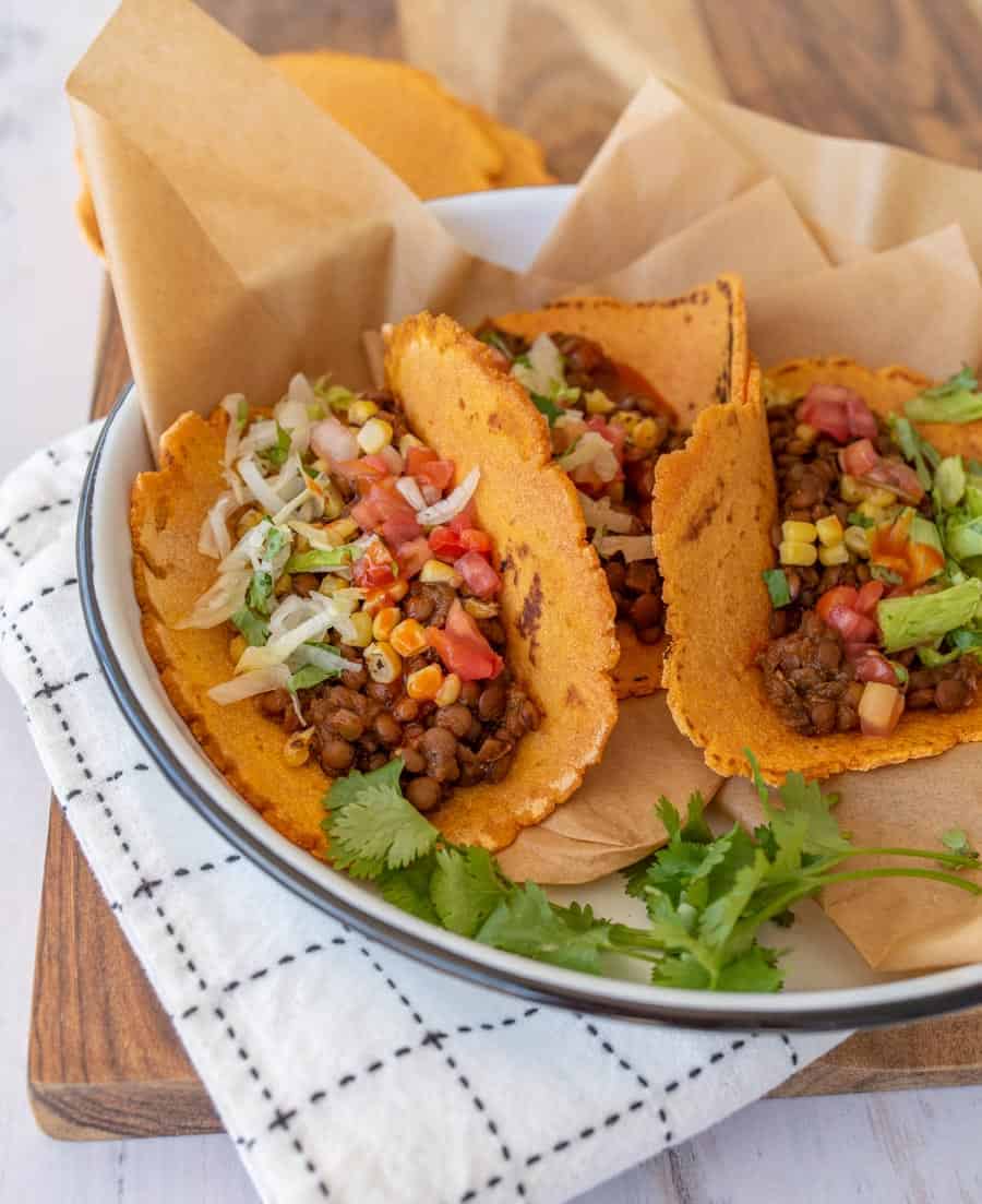 Close up of three sweet potato tortillas with lentil taco filling on parchment paper in a white enamelware pan with a black rim.