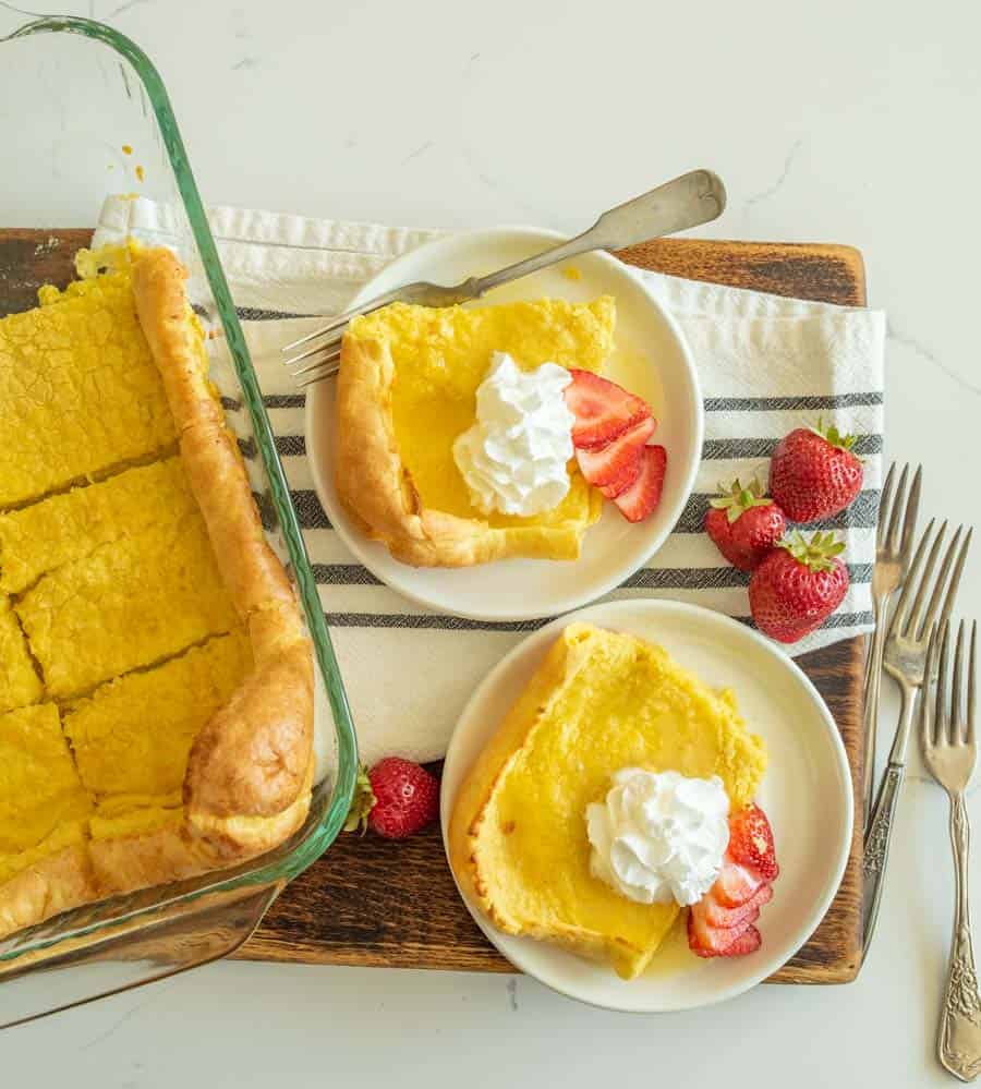 german pancakes cut and served on white plate with strawberries and whipped cream on top.