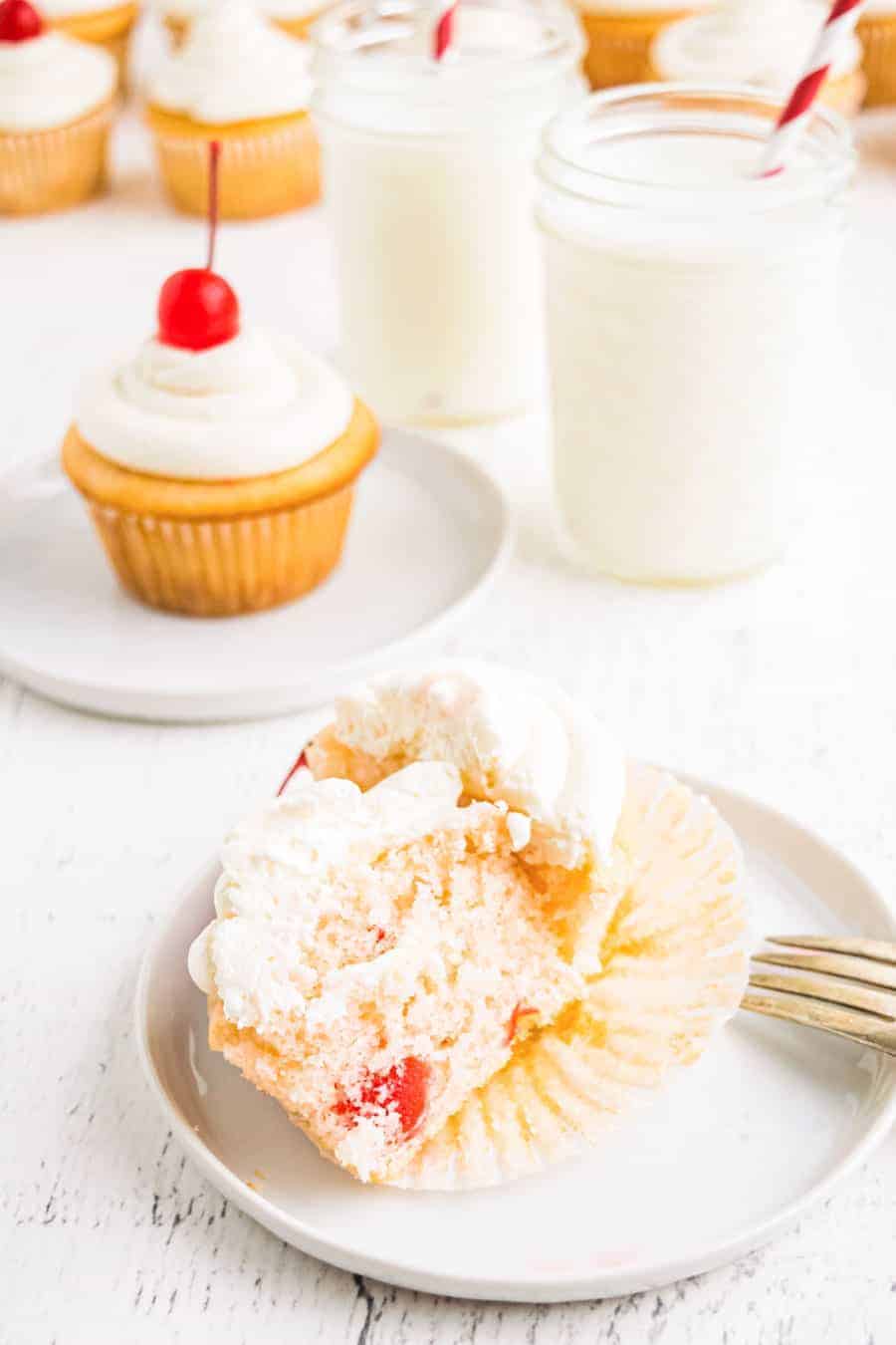Homemade cherry cupcake on a white plate cut in half on a white counter.