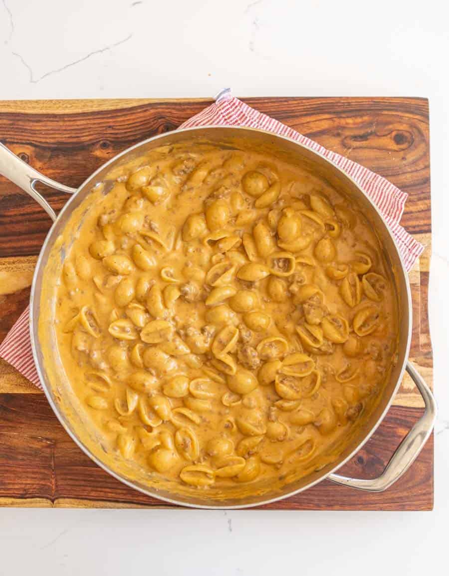 Cheesy pasta and beef in a skillet sitting on a wooden cutting board.