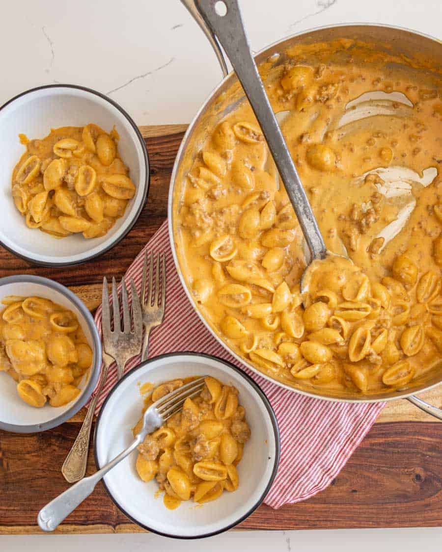 Hamburger helper being served into three white bowls on a wooden cutting board.