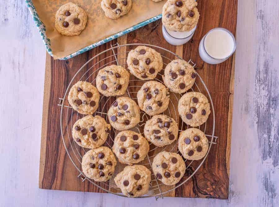 baked sourdough chocolate chip cookies on a cooling rack with glassed of milk next to them.