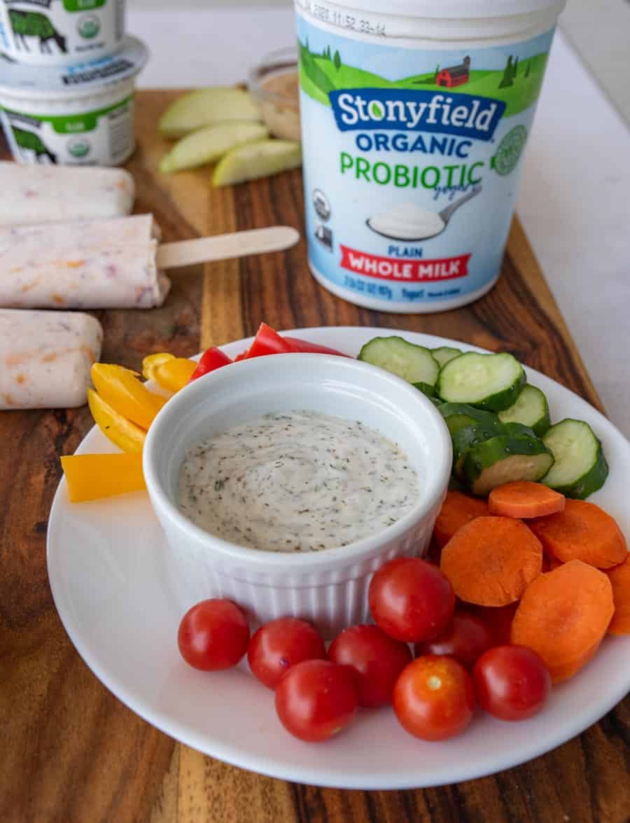 Close-up of veggies and dip including cucumber slices, bell pepper pieces, carrot rounds, and cherry tomatoes.
