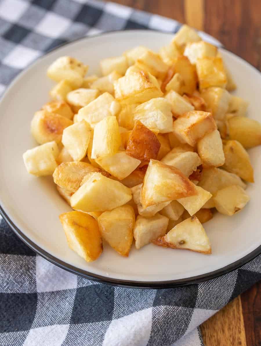 Crispy oven roasted potato cubes on a white enamel plate on a black and white gingham tablecloth.