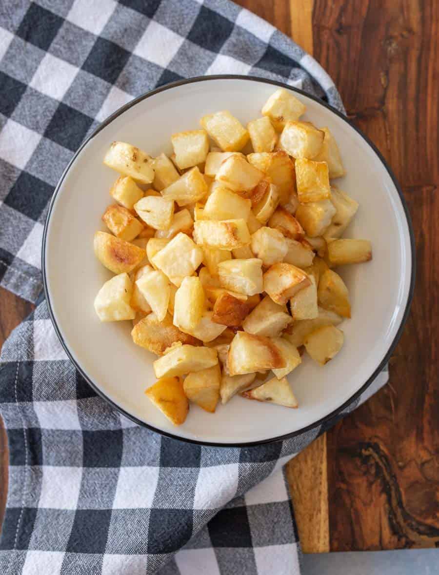 Crispy oven roasted potato cubes on a white enamel plate with a black rim on a black and white gingham tablecloth.