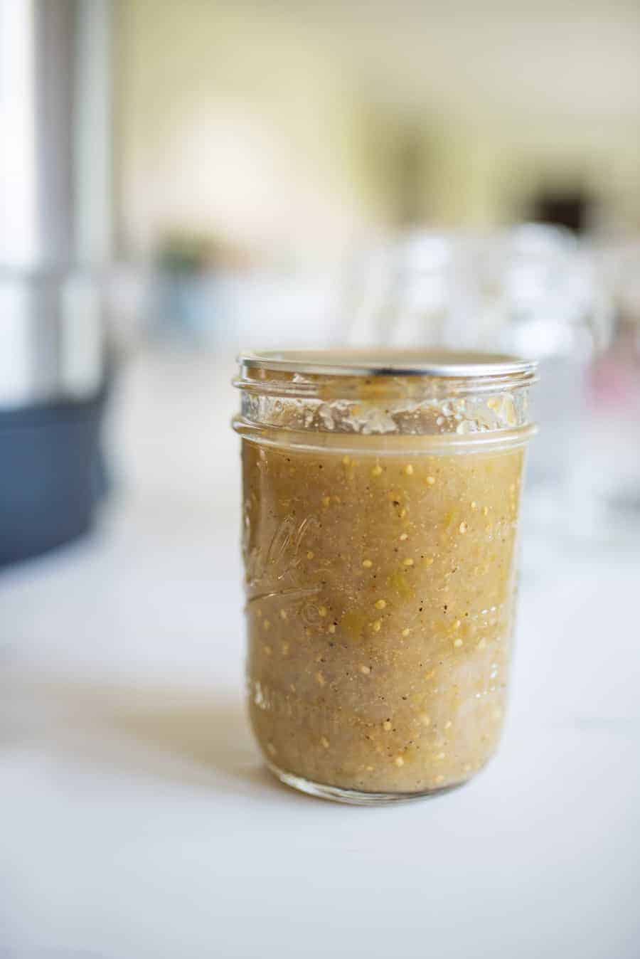 Close-up of one jar of green tomatillo salsa in a clear glass jar.