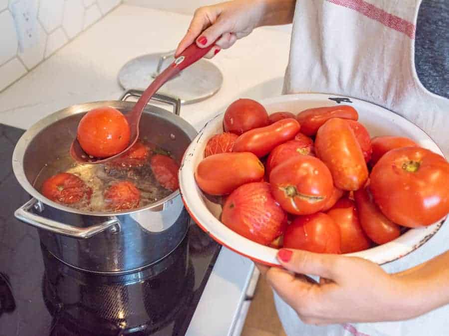 spoon removing blanched tomato from water bath.
