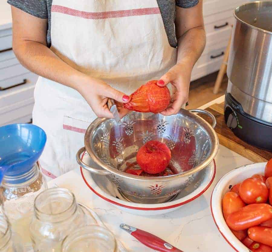 woman peeling skin from blanched tomatoes.