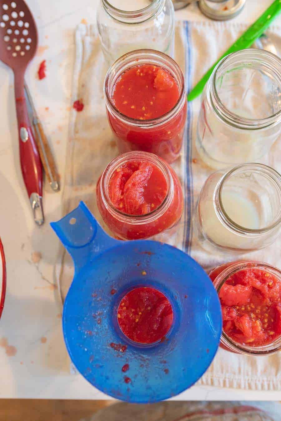 jars being filling with tomatoes for canning