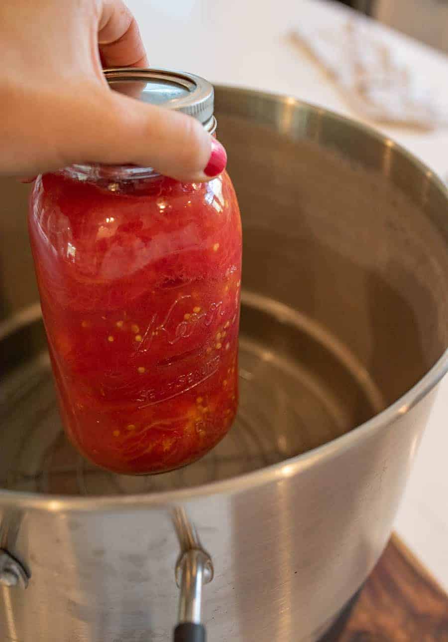 jar of tomatoes being lowered into water bath canner.