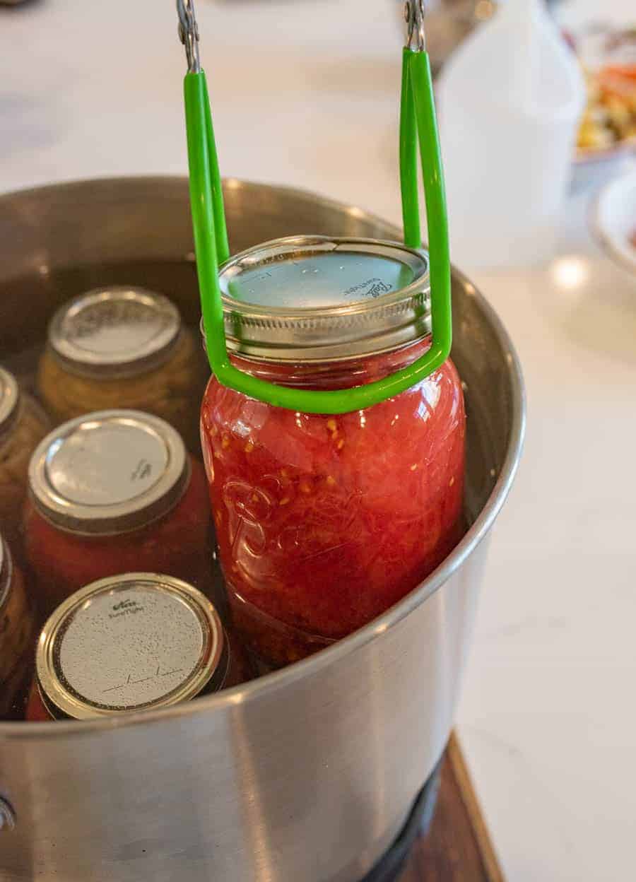 tongs being used to pull hot finished jar from water bath canner.