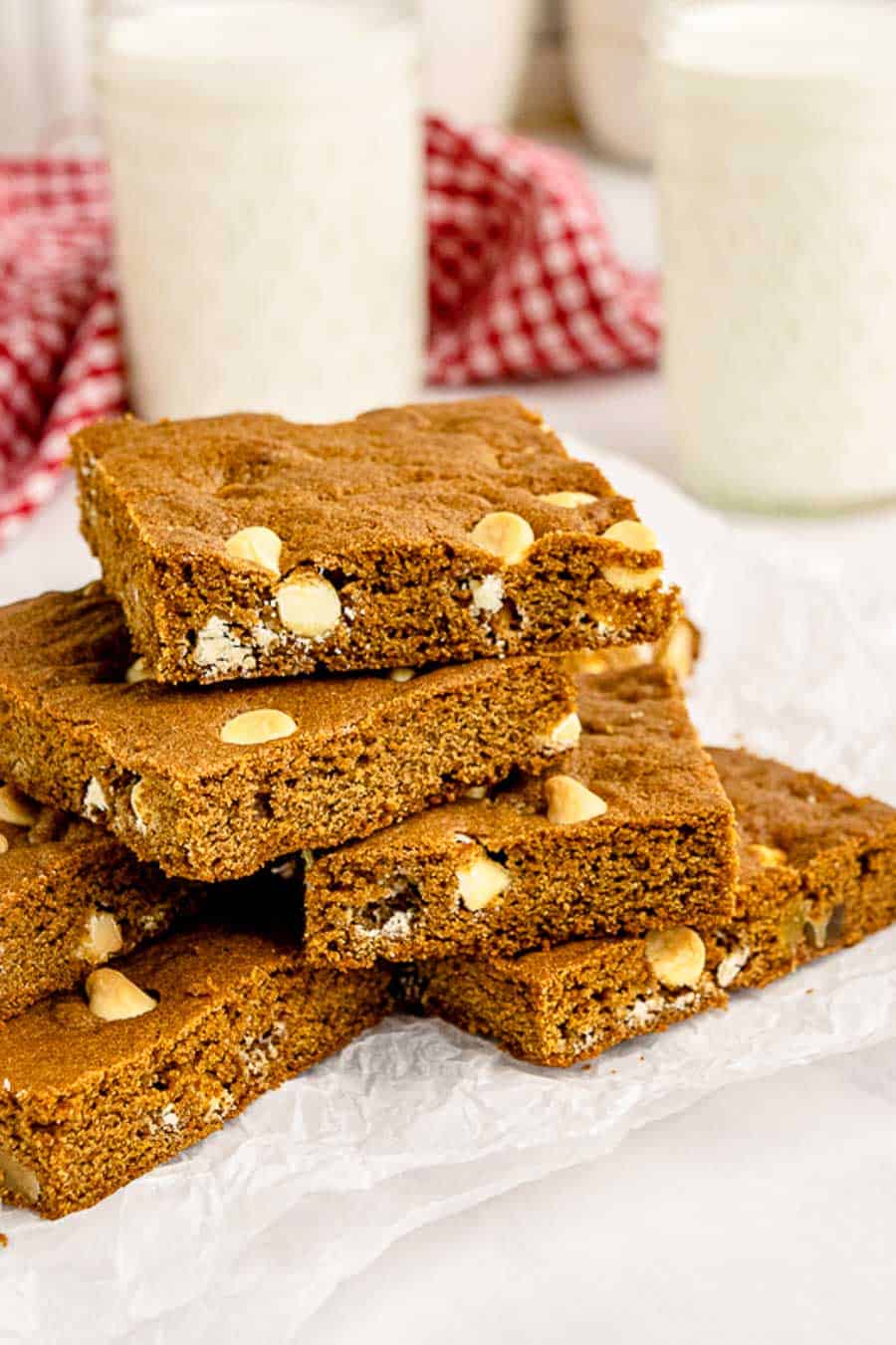 A pile of gingerbread blondies on a white plate with two glasses of milk in the background.