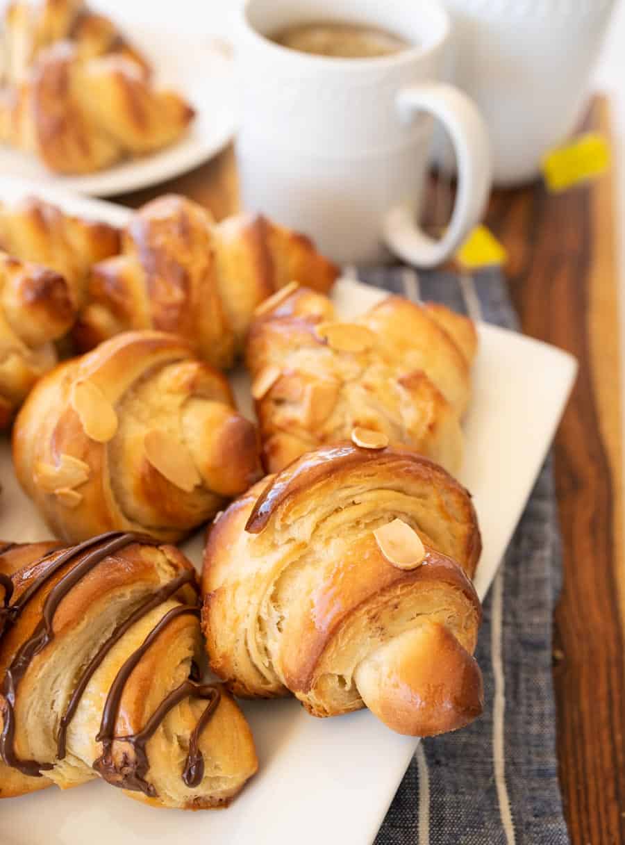 A close up of three kinds of croissants on a white plate with tea.