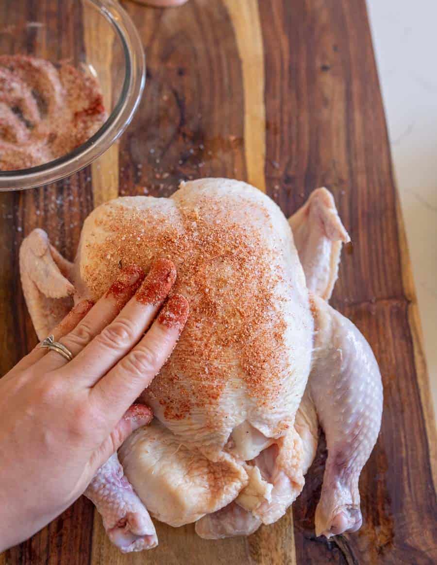 A hand rubbing the spice mixture onto the skin of a whole raw chicken.