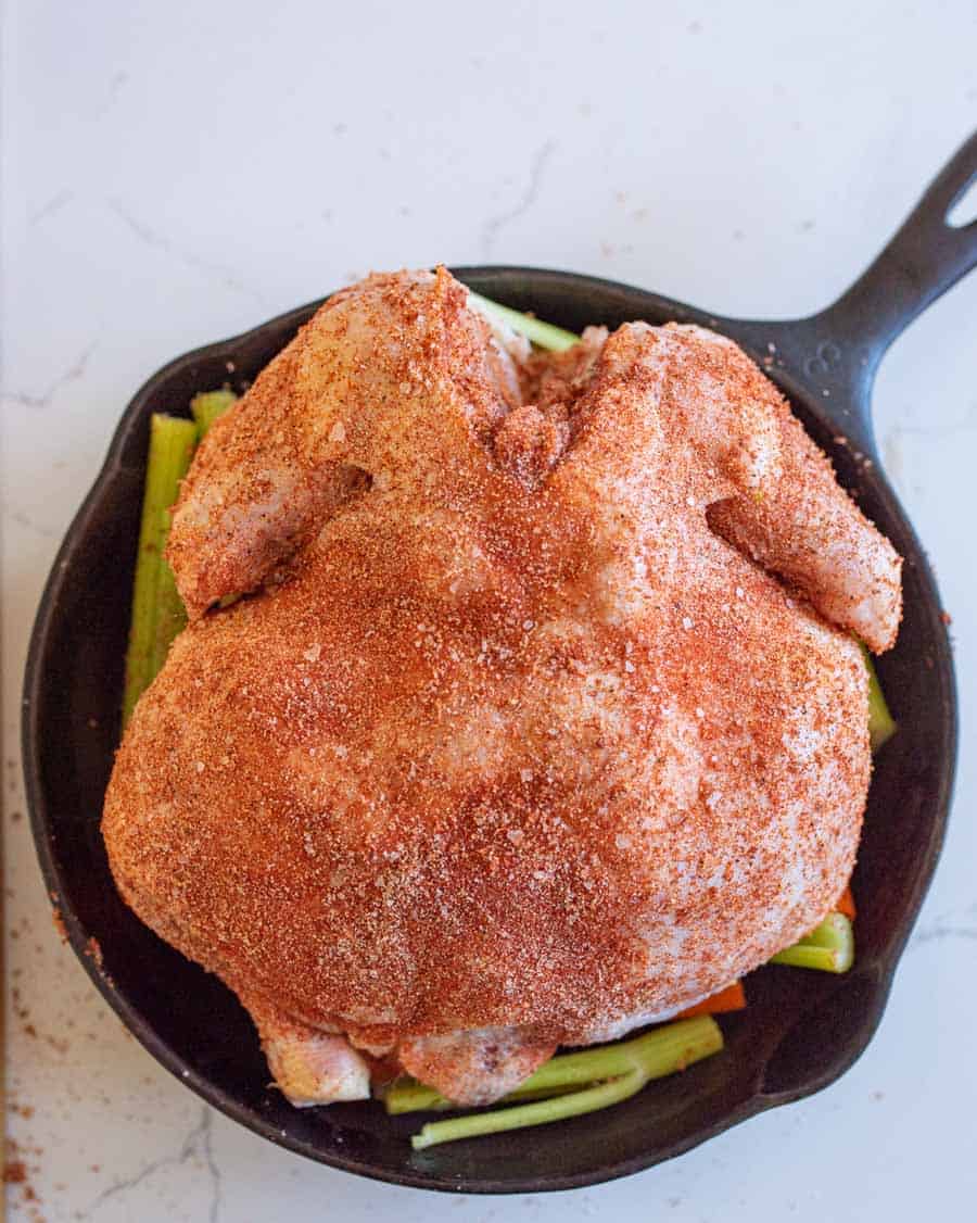 A whole raw chicken in cast iron skillet ready to be roasted in the oven.