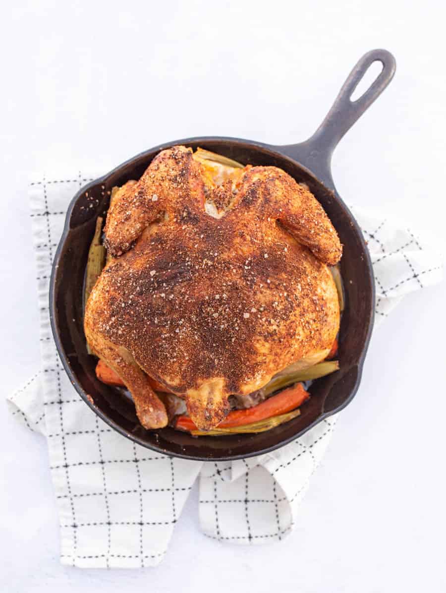 A whole roasted chicken in a cast iron skillet resting on a white and black towel.