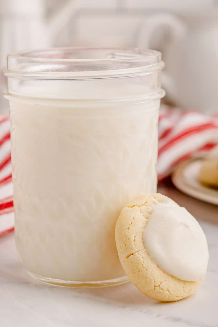 A baked and iced melt away cookie leaning against a glass of milk.