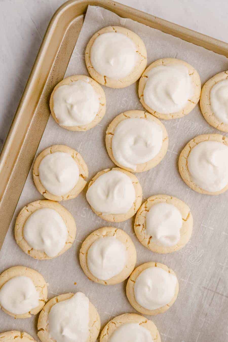 15 baked melt away cookies with icing on a baking sheet lined with parchment paper.